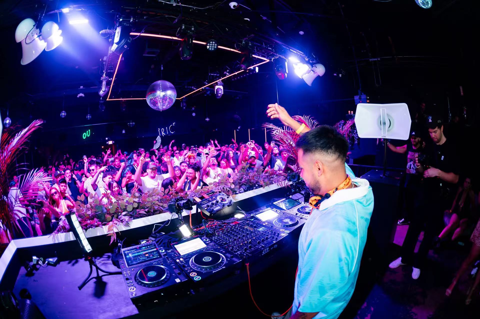 A DJ and dance-floor crowd under purple and blue lights.