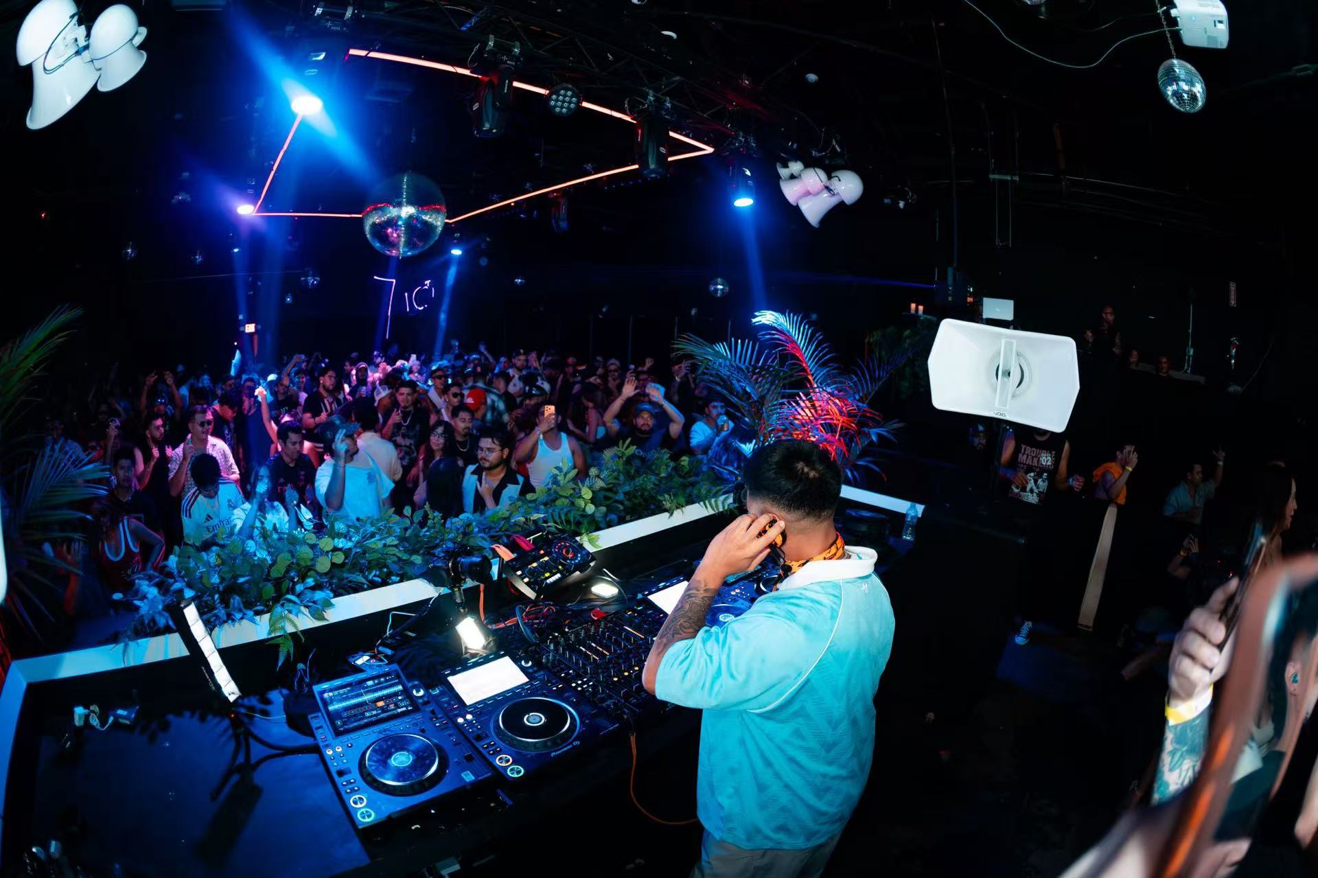 Side view of a DJ holding a headphone to one ear while facing a blue-lit crowd.