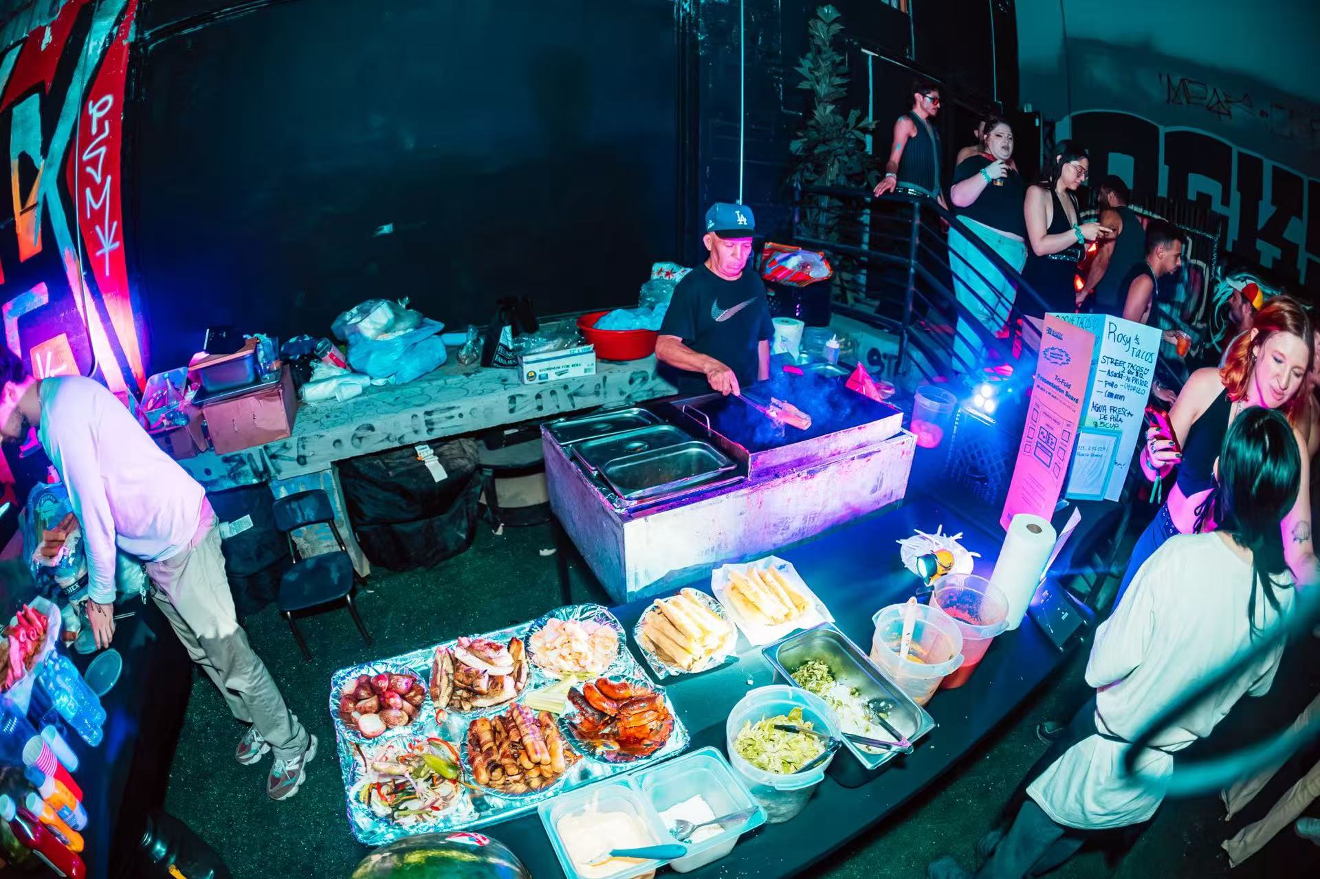 A food counter with trays of prepared food and guests gathered nearby.